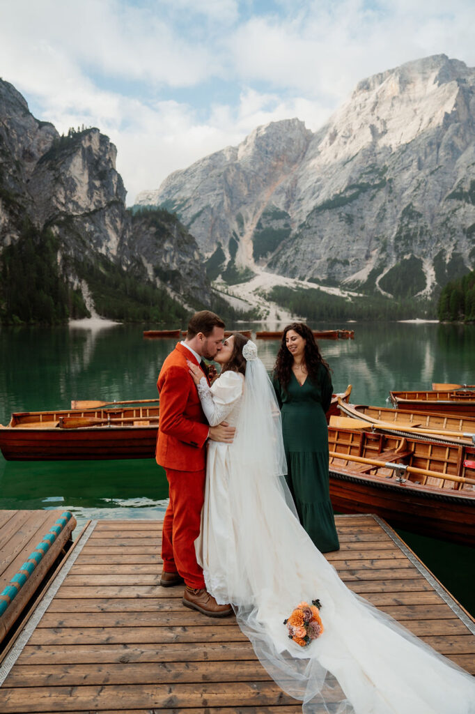 bride and groom kisses on a dock by Lago di Braies, surrounded by dolomites mountains in italy.