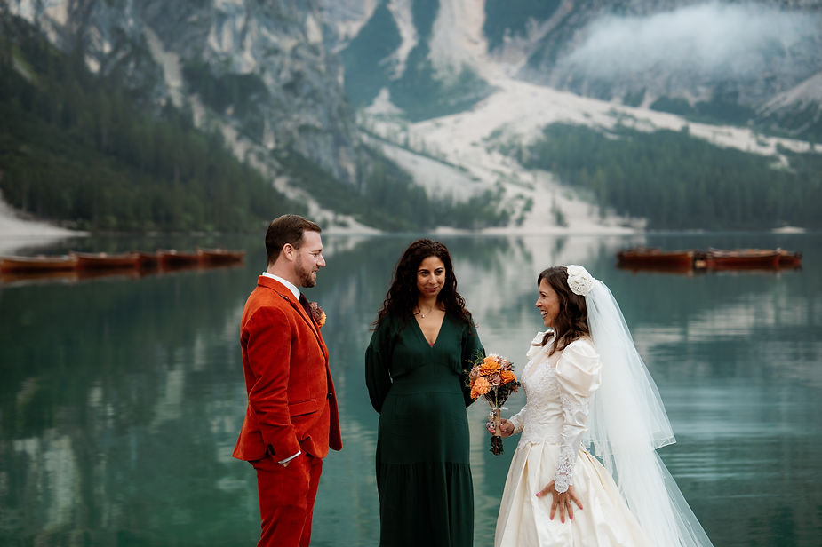 Bride and groom in vintage attire exchange elopement vows by a serene lake surrounded by mountains at Lago di Braies