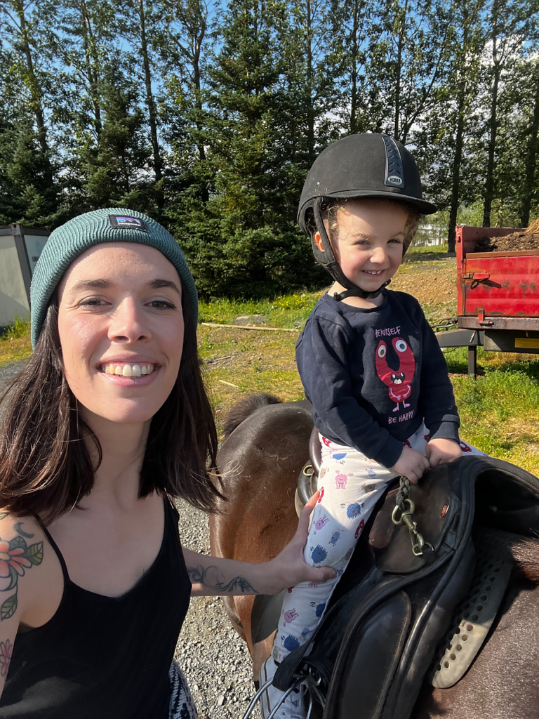 mom stands beside her kid riding on a small horse in iceland