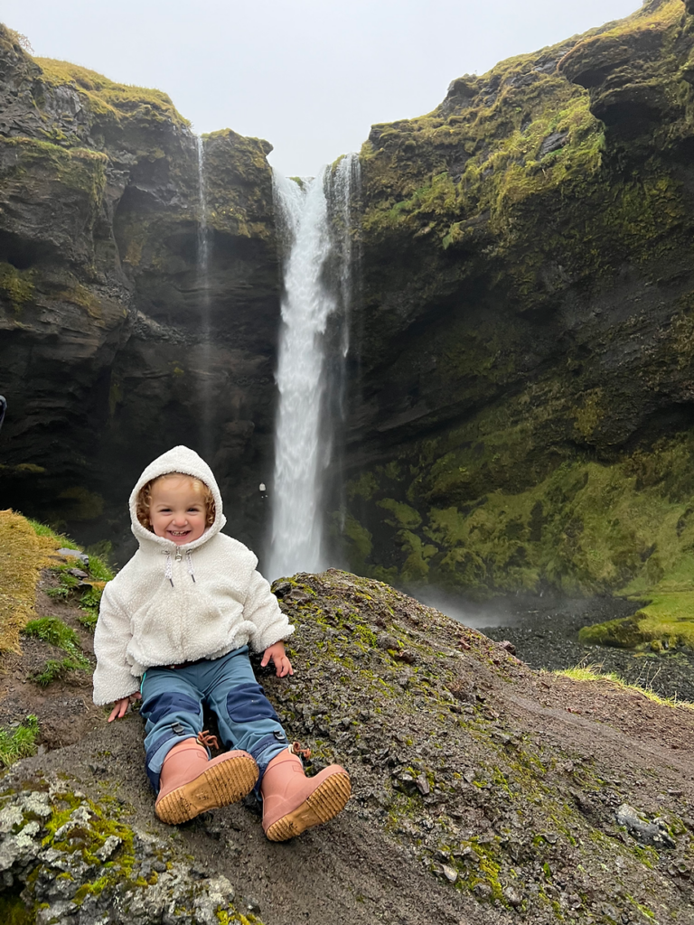 small child sits on rock with iceland waterfall in the background.