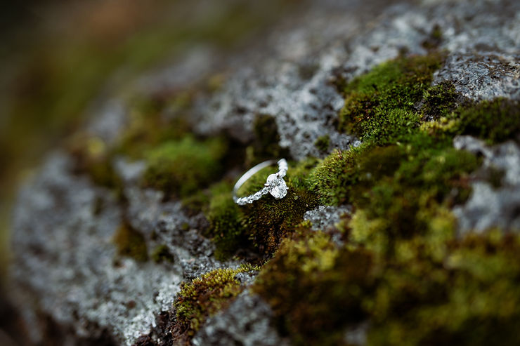 iconic iceland wedding locations: A diamond ring with a twisted band rests on moss-covered rock, highlighting a mix of green and gray textures in a natural setting.