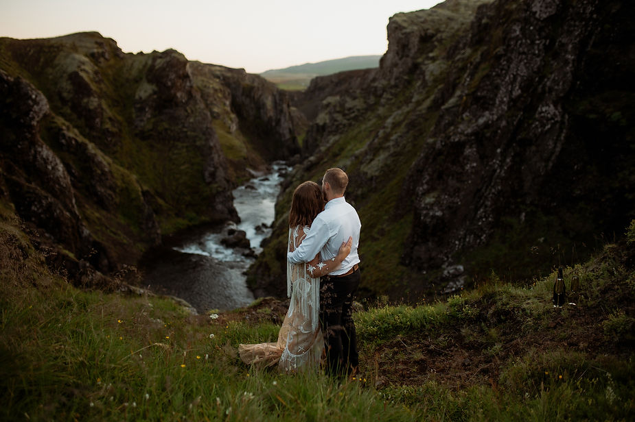Secret Iceland Elopement Spots: bride and groom embracing on grassy hill overlooking a canyon and river.