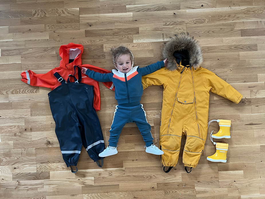 a child lays on the floor with outfits on either side of her before going on a hike in iceland