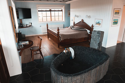 in iceland wedding venue, cozy bedroom with a wooden bed, stone bathtub, and blue walls. Window view, chair, table with glasses. Relaxing mood.