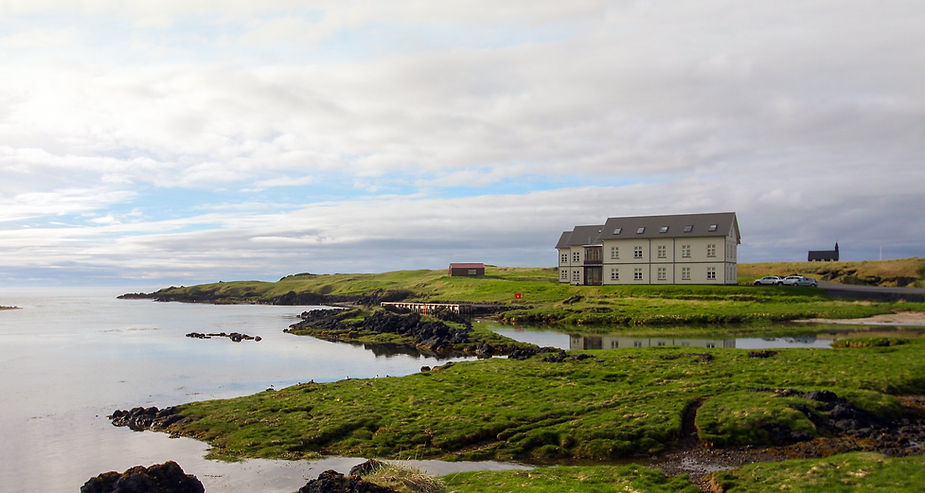 iceland wedding venue sits by a calm shore, surrounded by green grass and rocky landscape under a cloudy sky. Peaceful, natural setting.