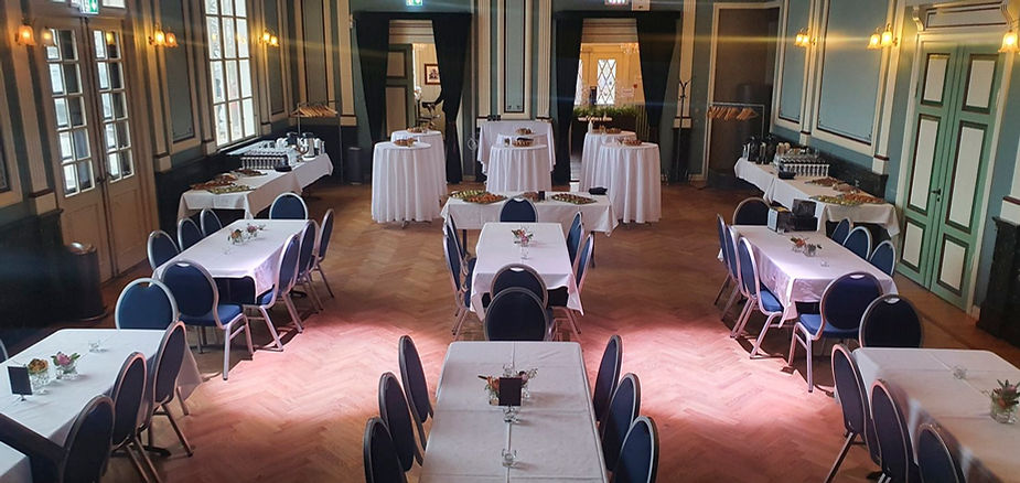 Elegant iceland wedding venue with round and rectangular tables set with white tablecloths, blue chairs, and floral centerpieces. Warm lighting and wooden floor.