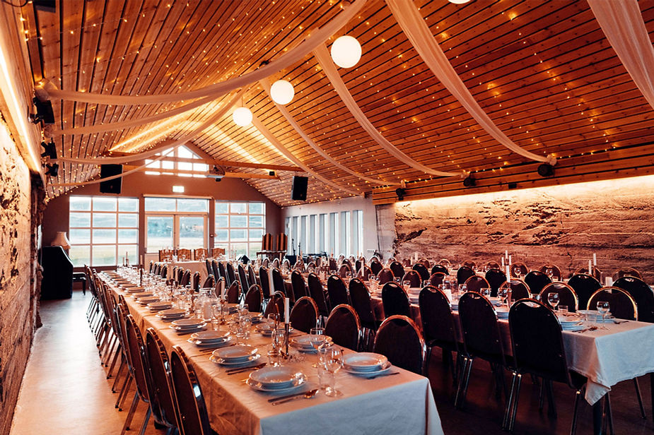 Elegant iceland wedding venue with long, set tables, overhead string lights, and wooden ceiling. Warm ambiance with a rustic stone wall background.