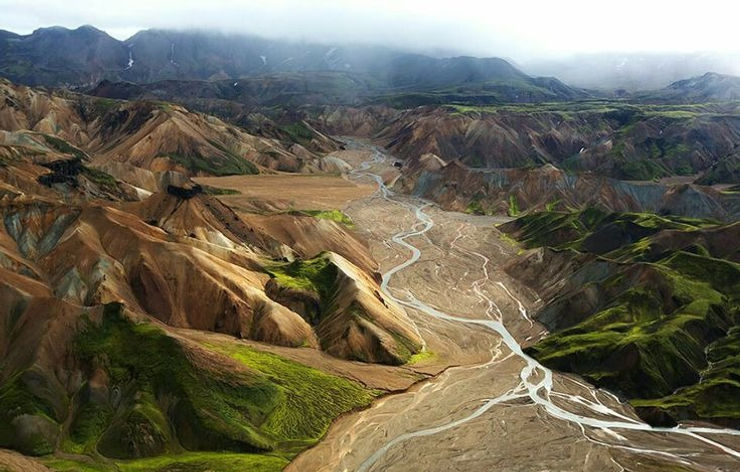 iconic iceland wedding location: Aerial view of colorful mountains with winding rivers in a lush green landscape, under cloudy skies. Rugged and serene natural scene.