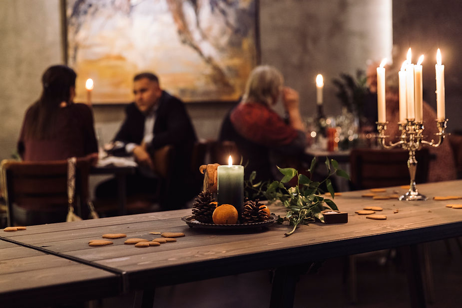 Dimly lit wedding venue in iceland with people dining, candles on tables, and a centerpiece with pinecones and greenery on a wooden surface, creating a cozy ambiance.