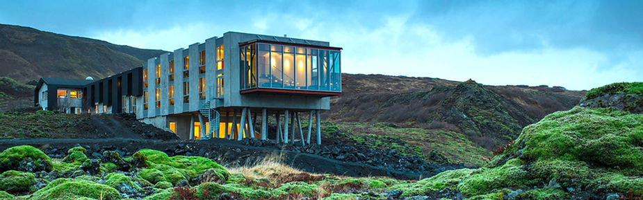 iceland wedding venue with large windows and glowing interior, set in a mossy, rocky landscape under a cloudy sky. Tranquil mood.