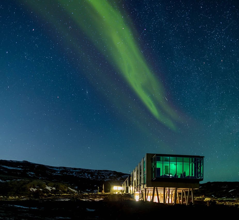 Aurora borealis over an iceland wedding venue with large windows, set against a starry night sky. The building glows green, creating a serene mood.