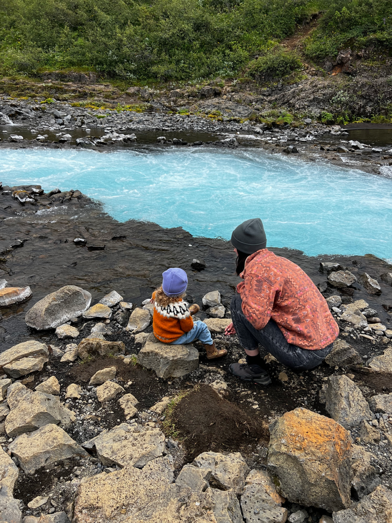 mother bends down while at a stream with her kid in iceland