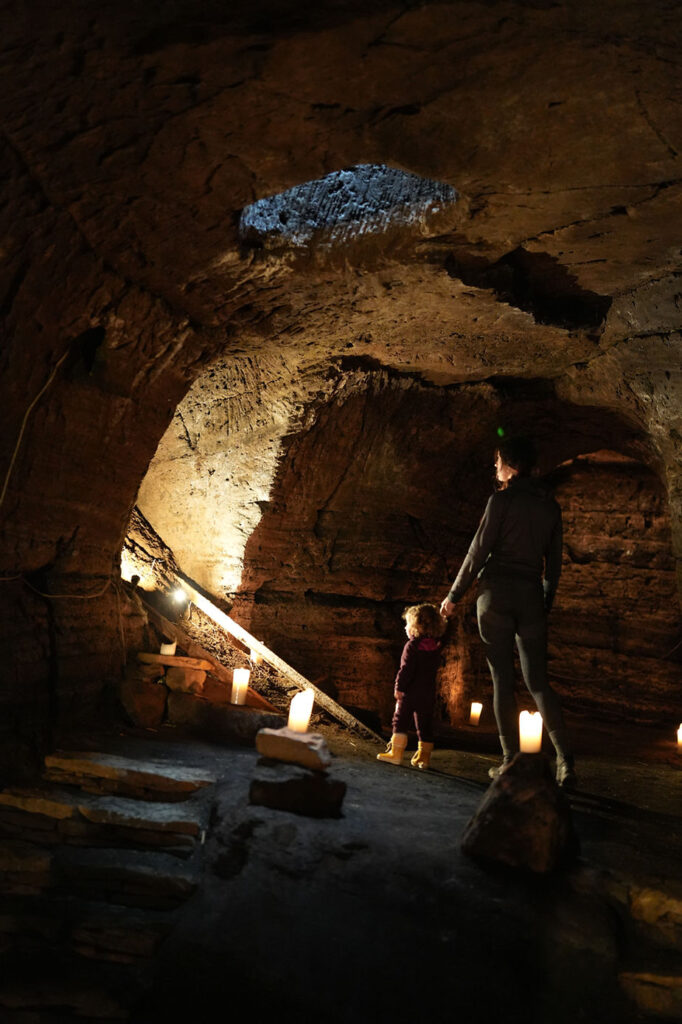 Adult and child exploring a candle-lit cave in iceland. They stand on a rocky floor, gazing at the illuminated walls. Warm, dim ambiance.