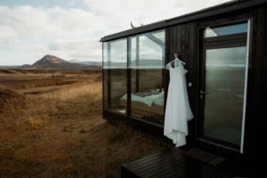 wedding dress hangs on the side of a glass cabin in iceland