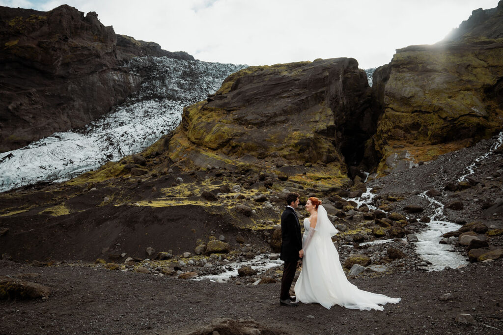 Bride and groom stand facing each other in a rocky, mountainous landscape with small streams during Ásatrú elopement ceremony