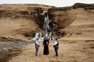 two grooms stand in front of waterfall during Ásatrú Ceremony in iceland