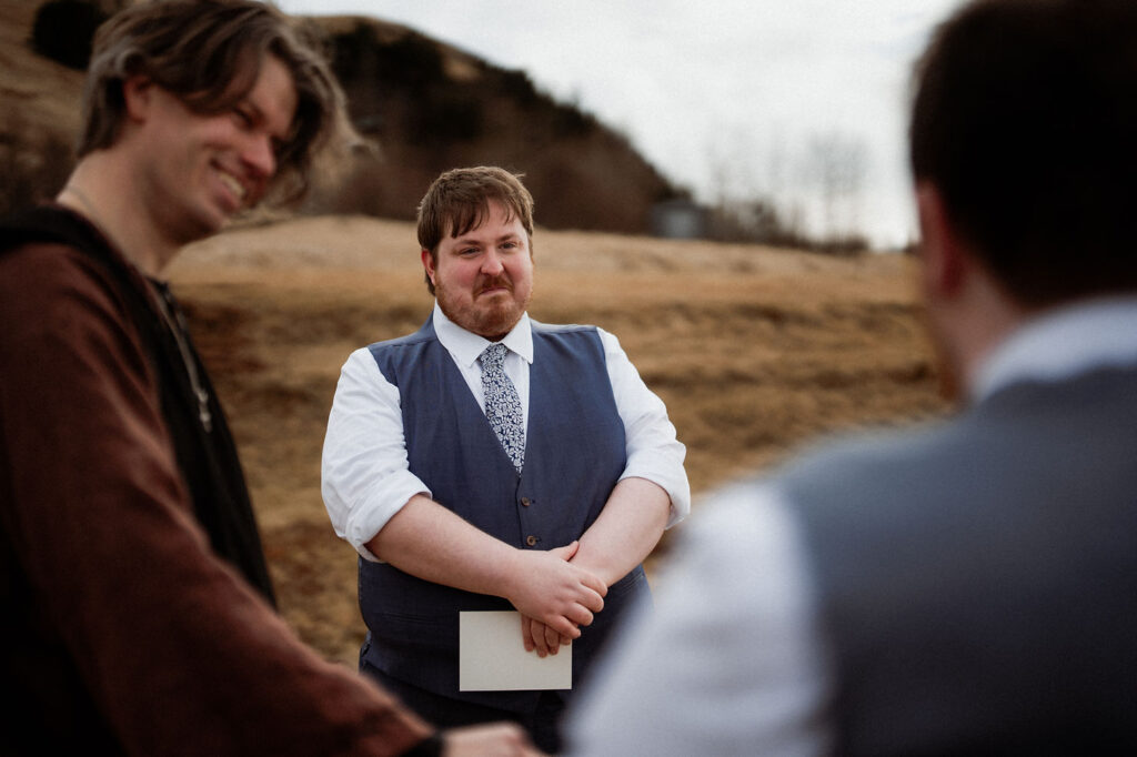 groom holds paper, looking serious as his groom says wedding vows during iceland elopement
