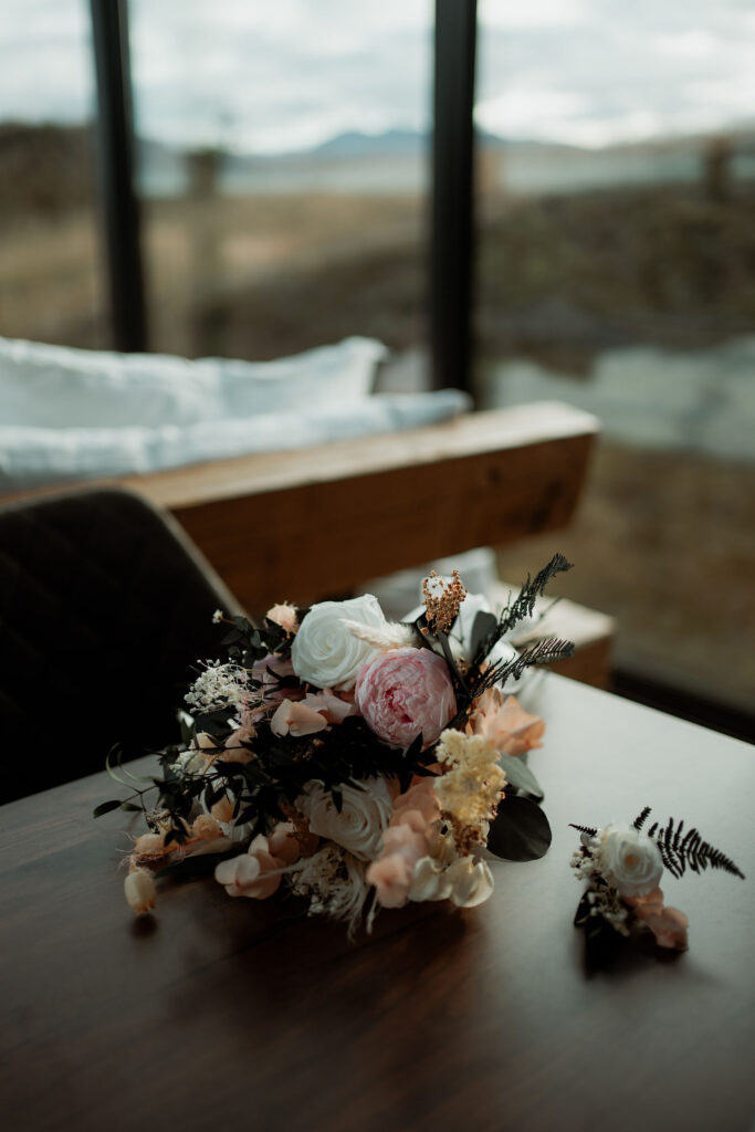 elopement bouquet of pink and white flowers on a wooden table with a blurred, scenic window view. 