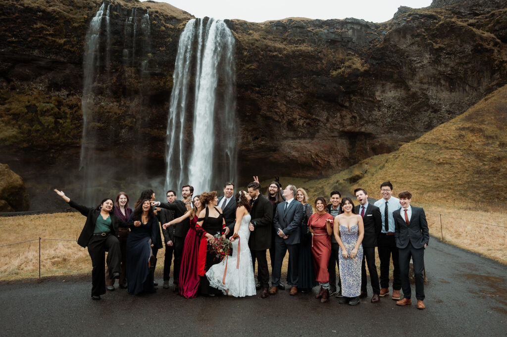 How to Include Your Family When You Elope: Group of people in formal attire celebrating by a waterfall, with joyful expressions.