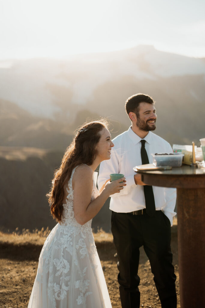 A couple in wedding attire smiles while holding cups outdoors, with a mountainous backdrop. Þórsmörk Valley in iceland