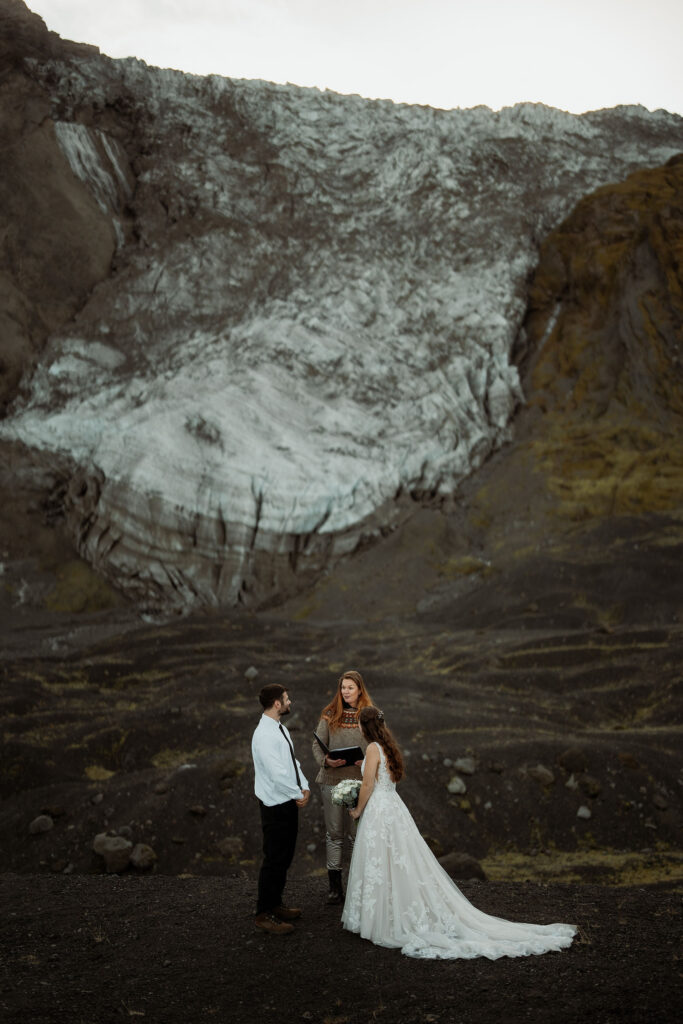 bride and groom exchange vows with an officiant in front of Þórsmörk Valley in iceland. 