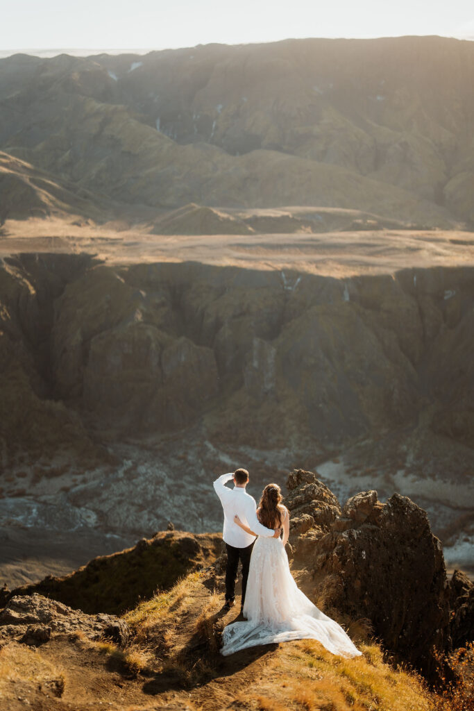 bride and groom during elopement stand on a rocky cliff, overlooking Þórsmörk Valley in iceland.