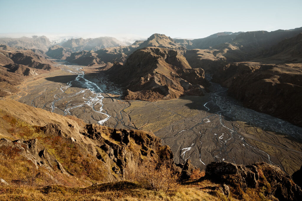 Mountain landscape with a winding river, brown and green terrain, and distant peaks under a clear blue sky. view of Þórsmörk Valley during elopement.