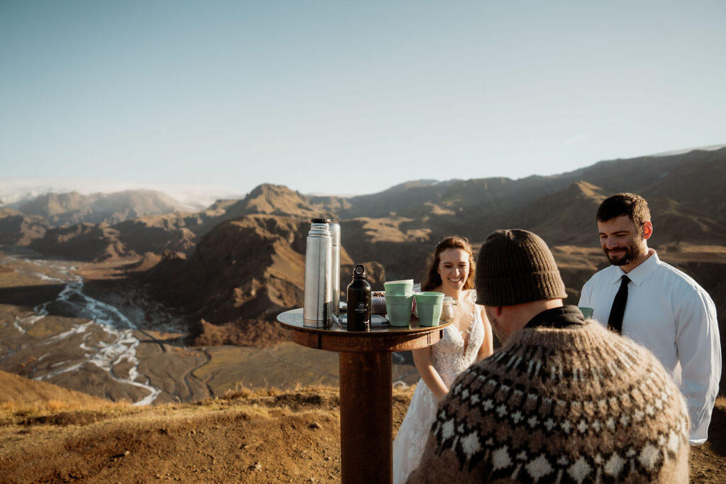 bride and groom smiling beside a table with mugs and thermoses on a mountain top under a clear sky. at Þórsmörk Valley during adventure elopement.