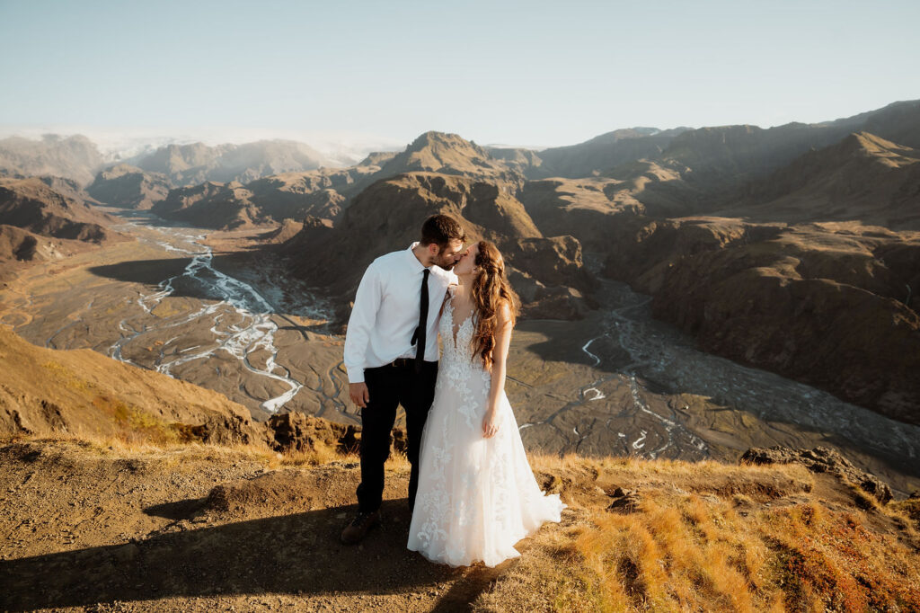 bride and groom kiss on a mountaintop at sunset, overlooking the Þórsmörk Valley with winding rivers during wedding adventure in iceland.