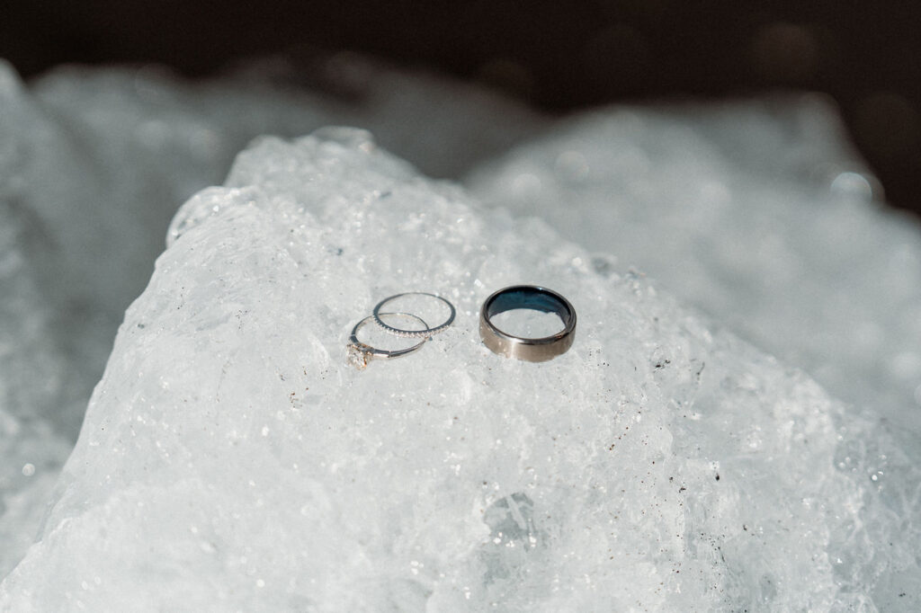 How to Include Your Family When You Elope: Two wedding rings and a silver ring rest on a block of ice. The ice sparkles in the sunlight.