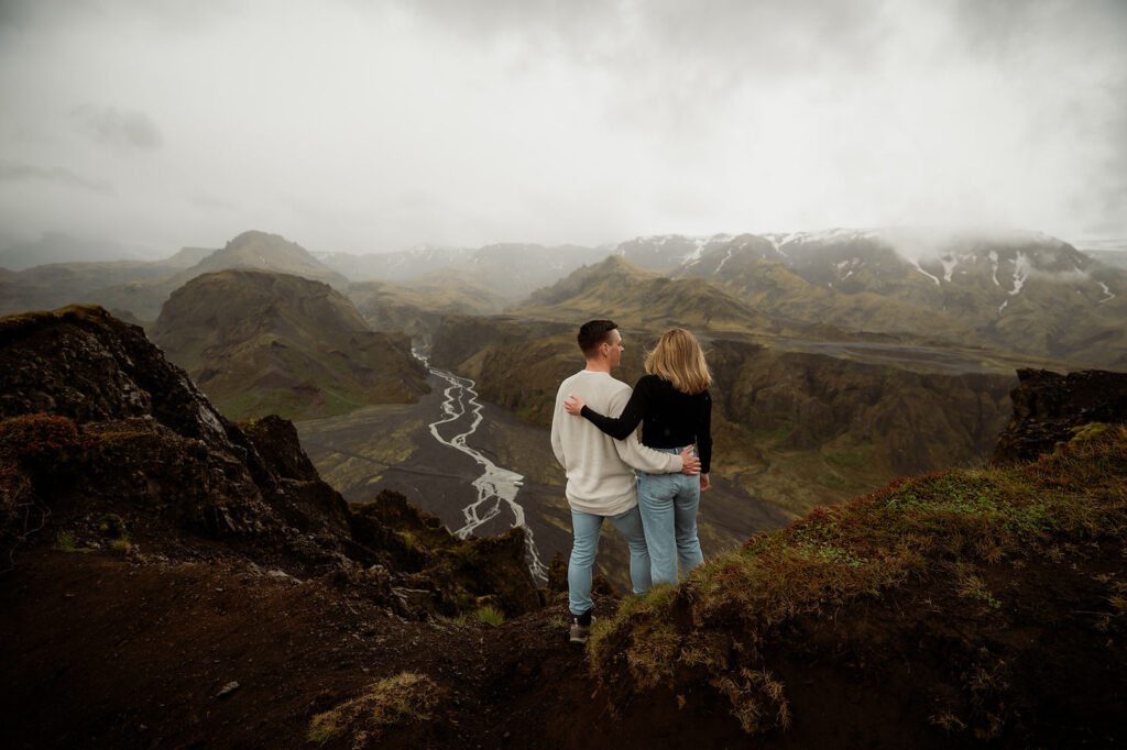 Couple embracing, overlooking a vast mountainous landscape with winding river at Þórsmörk Valley in iceland
