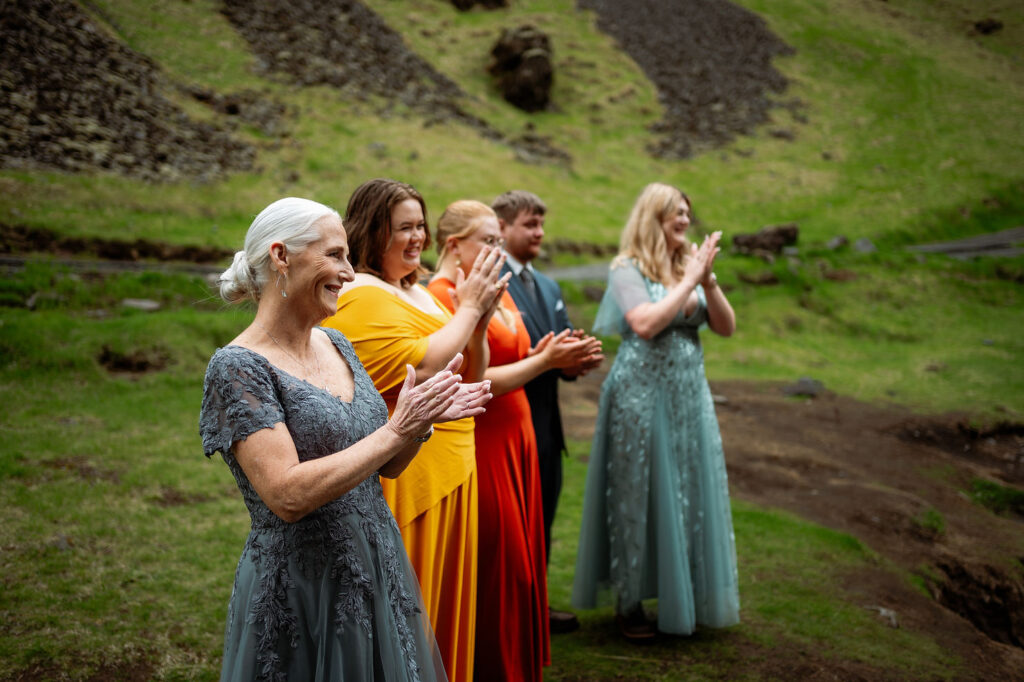 How to Include Your Family When You Elope: People in colorful formal wear clapping joyfully outdoors on grassy terrain.