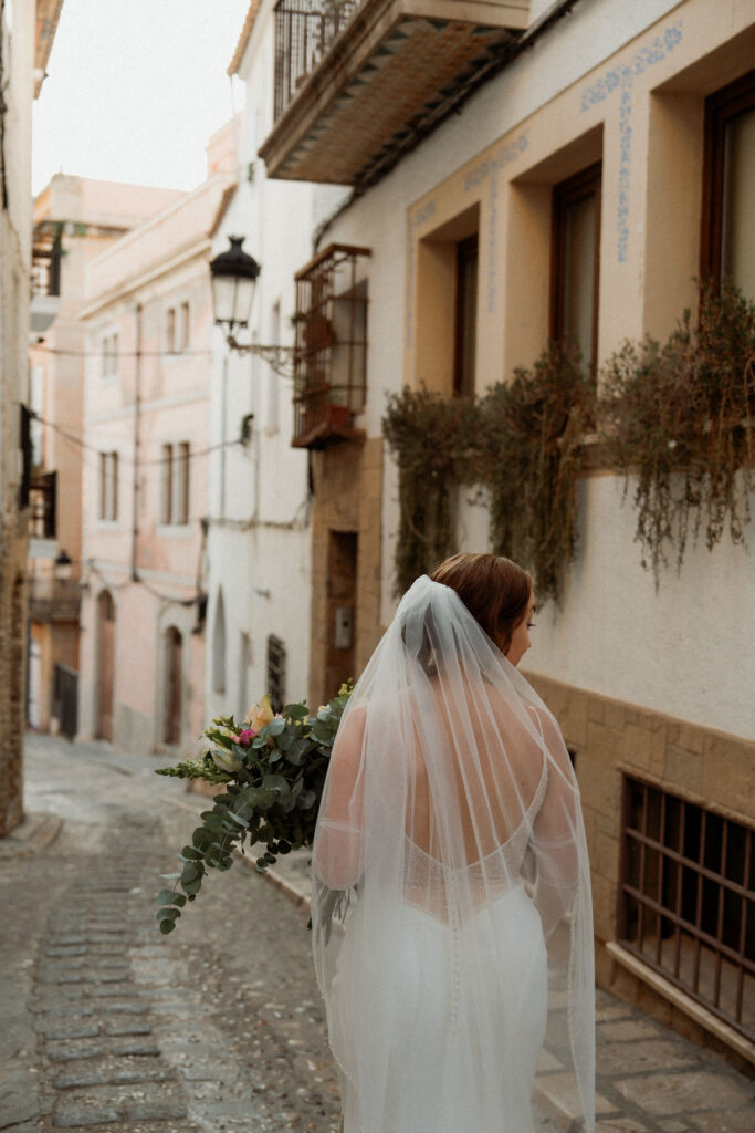 Bride holding flowers, walking down a narrow cobblestone in Barcelona.