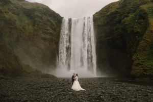 bride and groom stand in front of Skógafoss waterfall during iceland elopement