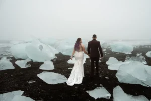 bride and groom hold hands and walk through ice chunks at diamond beach during iceland elopement