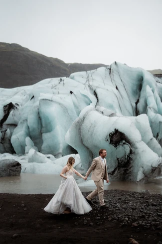 after figuring the cost of an iceland elopement, bride and groom hold hands and walk past glacier