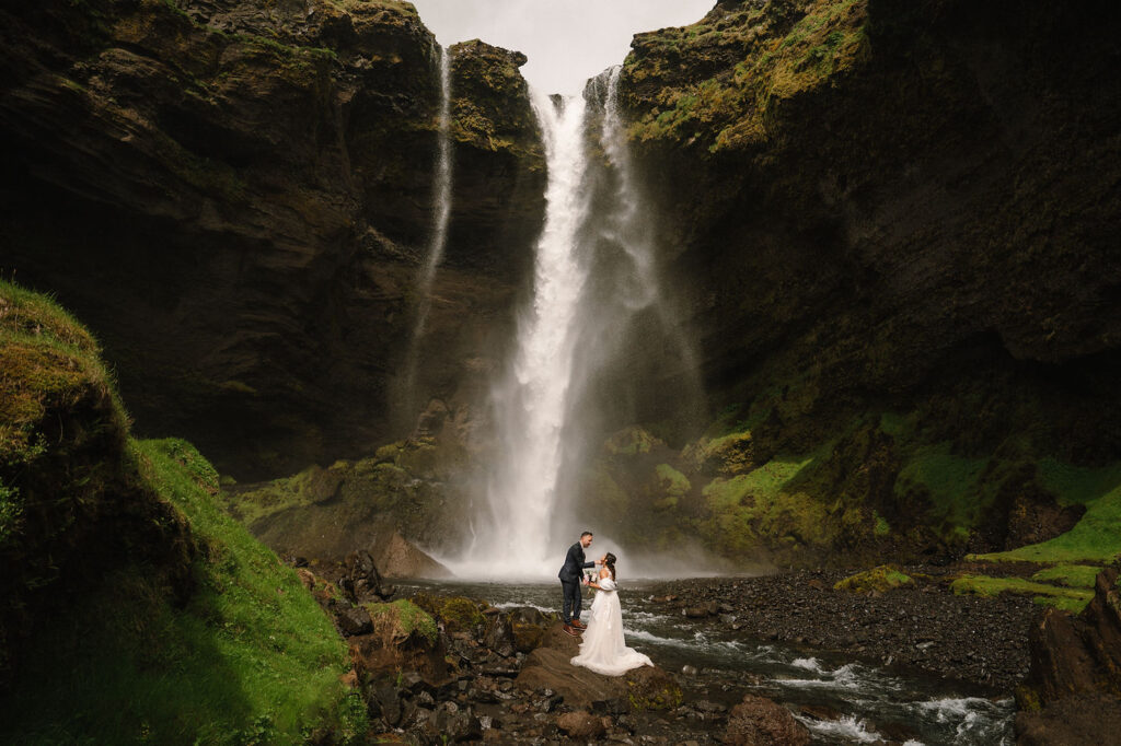 bride and groom stand at the base of kvernufoss waterfall, the best place to elope in iceland.