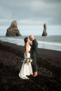 bride and groom stand on the black sand beach while holding their elopement bouquet