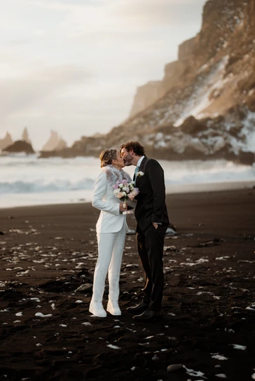 bride and groom kiss while standing on the black sand beach in iceland during elopement