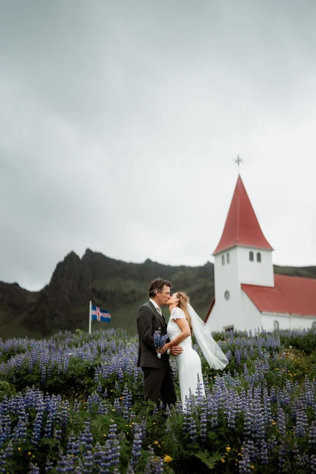 bride and groom stand in flower field in front of old church in iceland during elopement
