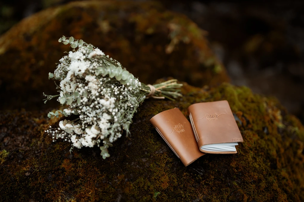 simple elopement bouquet sits on the ground beside some wedding vow books in iceland