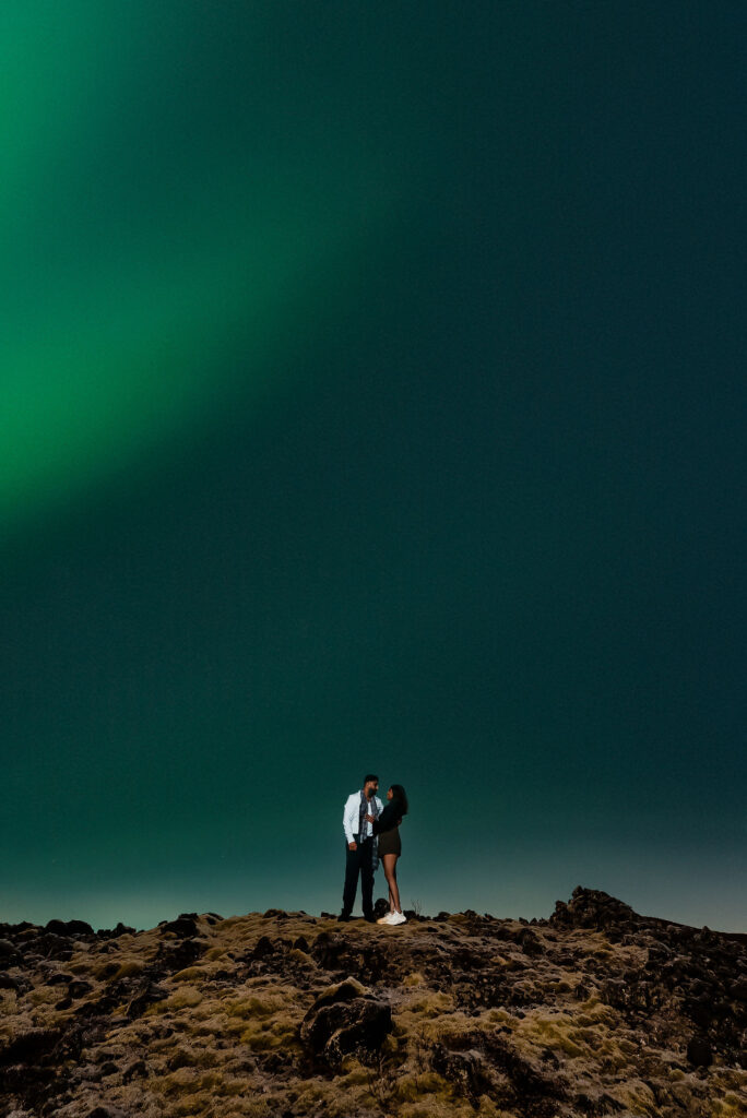 engaged couple leans on each other during photos for a northern lights proposal in iceland