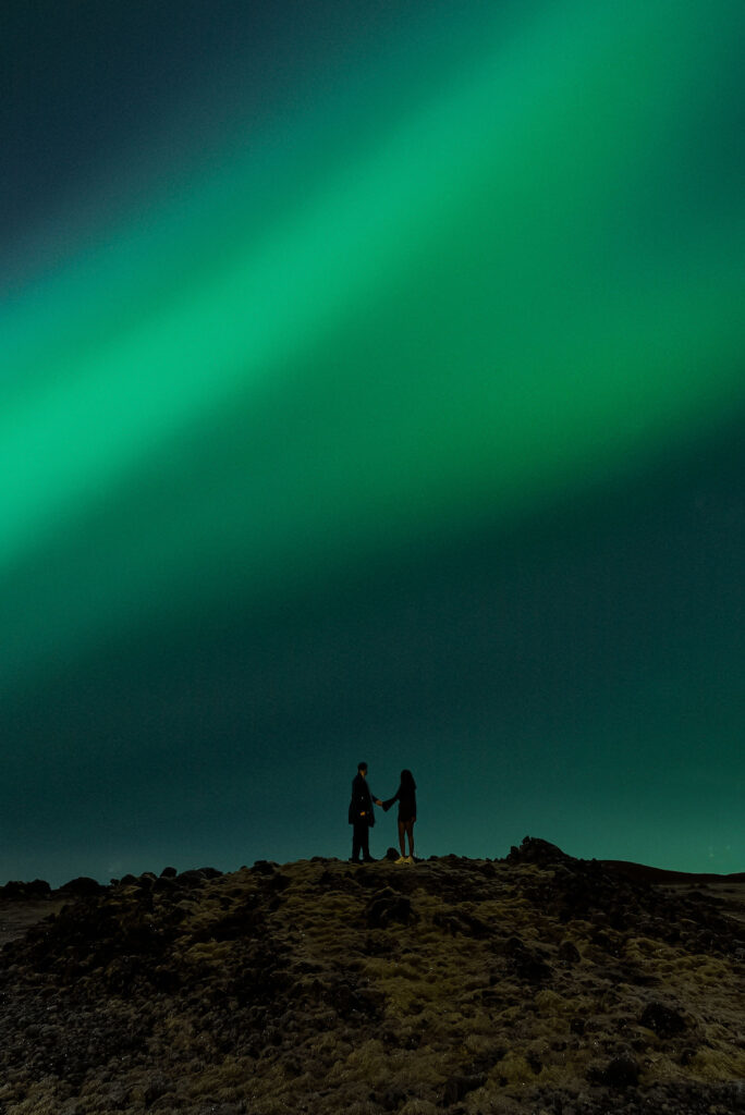 couple stands on hill during the aurora borealis proposal
