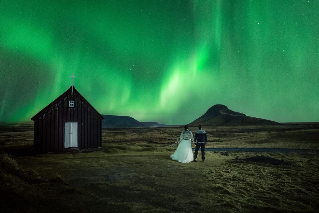 bride and groom hold hands and stand looking at the sky during northern lights elopement in iceland