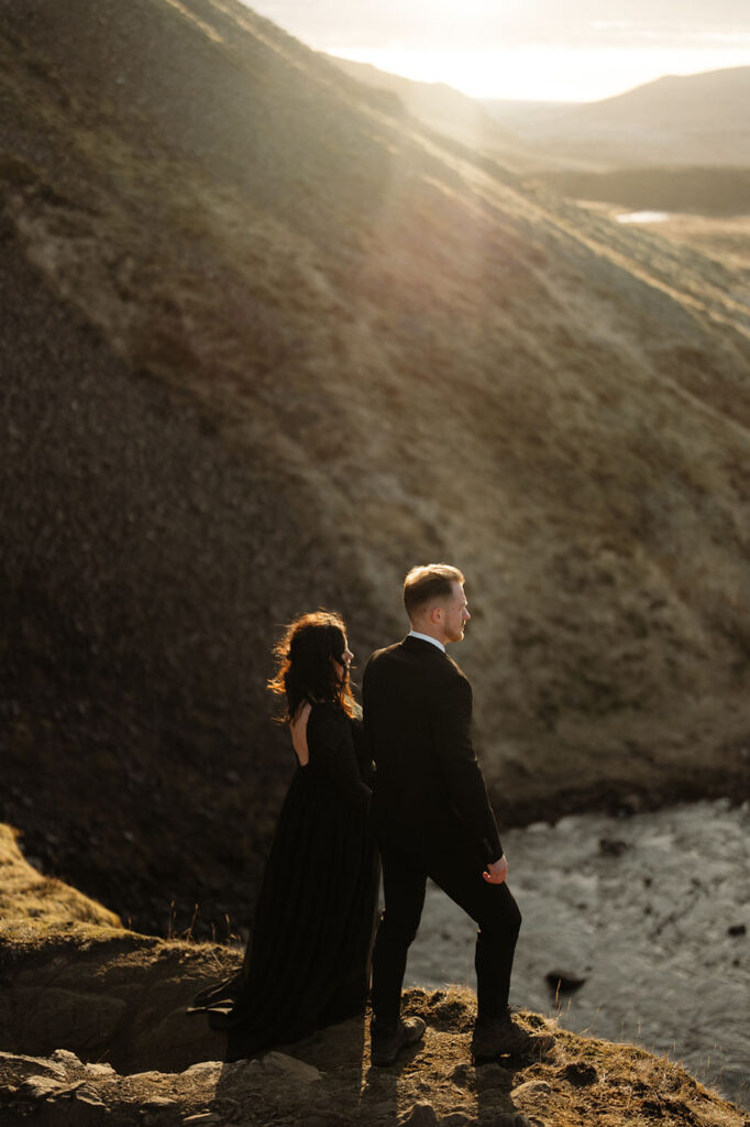 A couple stands overlooking the edge of a cliff during Sunset Elopement by Iceland Wedding Photographer, Lia Photo Stories.