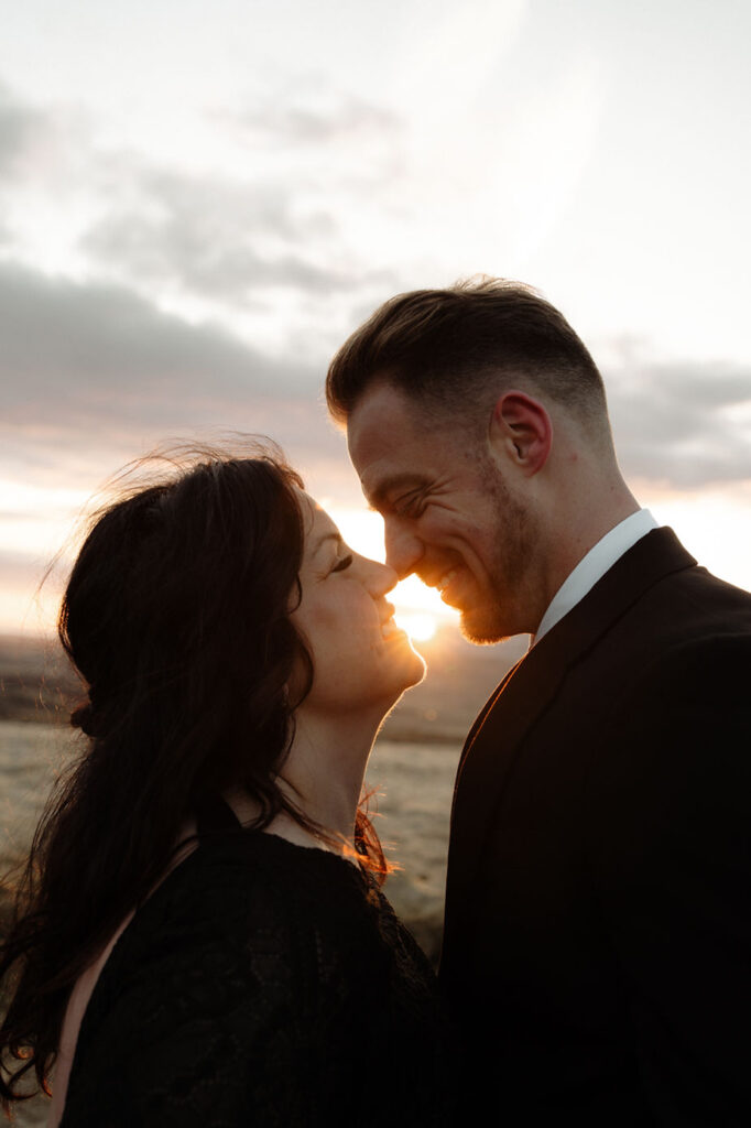 Iceland wedding photographer takes a photo of a bride and groom in black, nose to nose, with the sunset in the background.