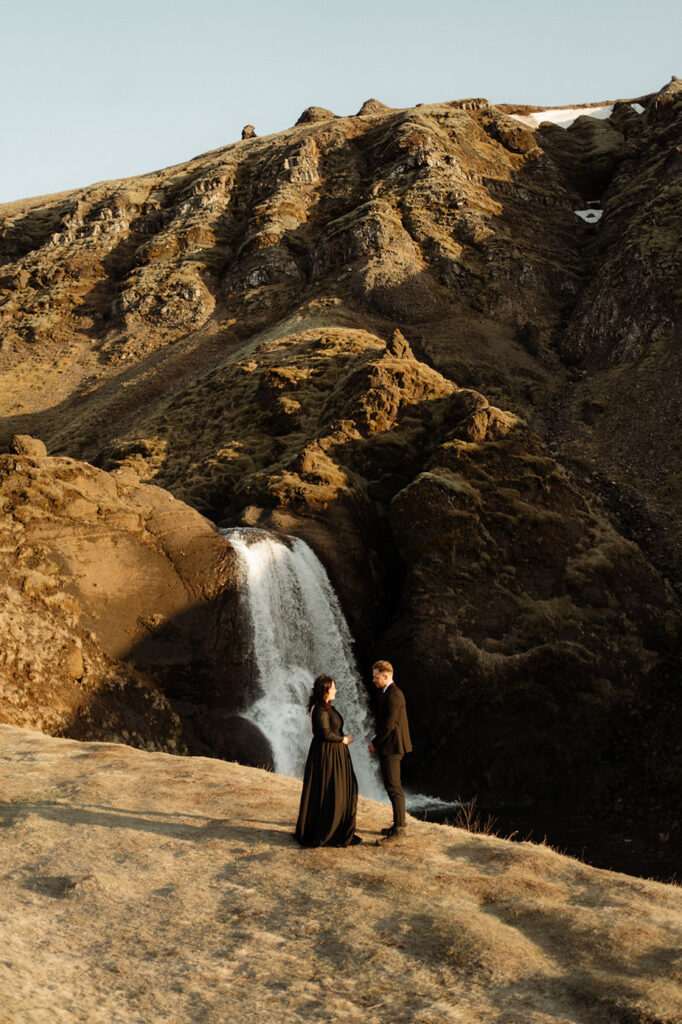 Bride and Groom stand with Helgufoss waterfall in the background as they say their vows during Sunset Elopement with Iceland Wedding Photographer, Lia Photo Stories.