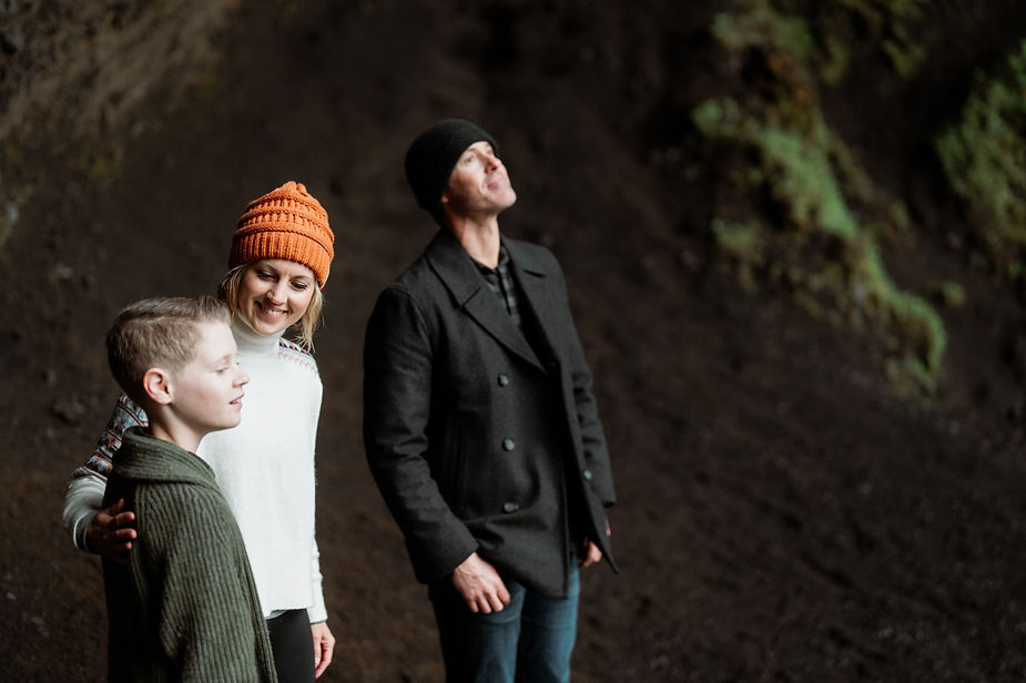 A family stands behind a waterfall during family photos by iceland elopement photographer.