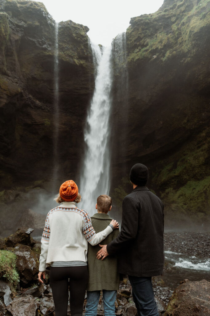 family looks at waterfall during Iceland family photo shoot.