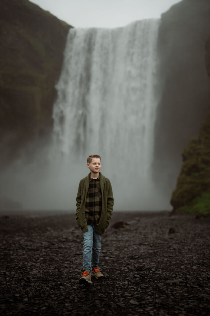 young boy walks in front of waterfall during family photos with iceland photographer.